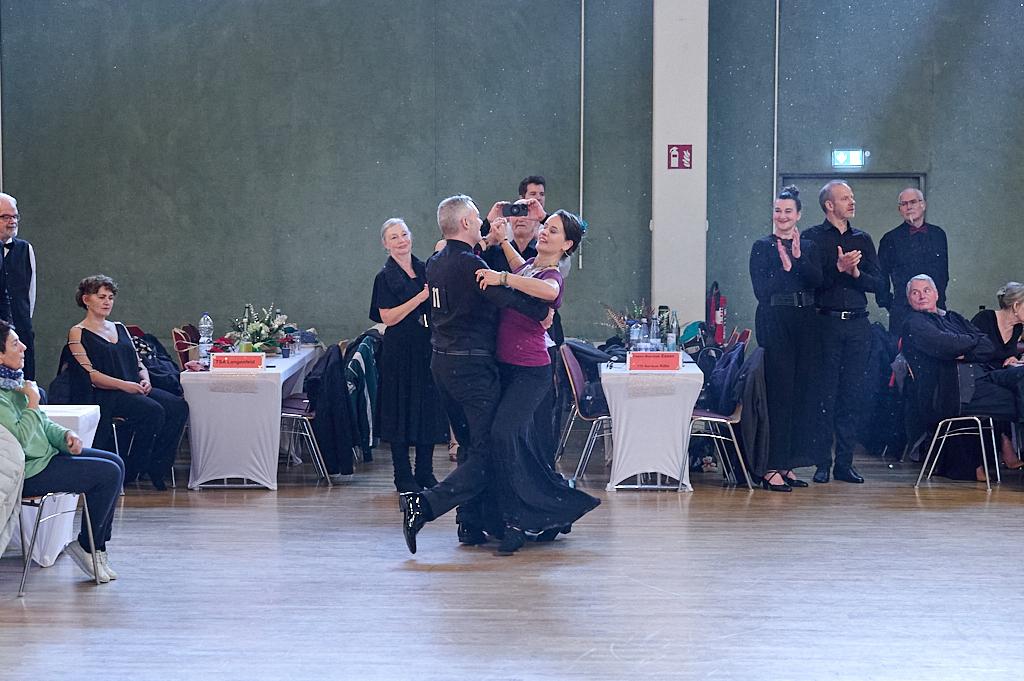 Tanzpaar in eleganter Kleidung tanzt auf einer Veranstaltung, Publikum applaudiert im Hintergrund.