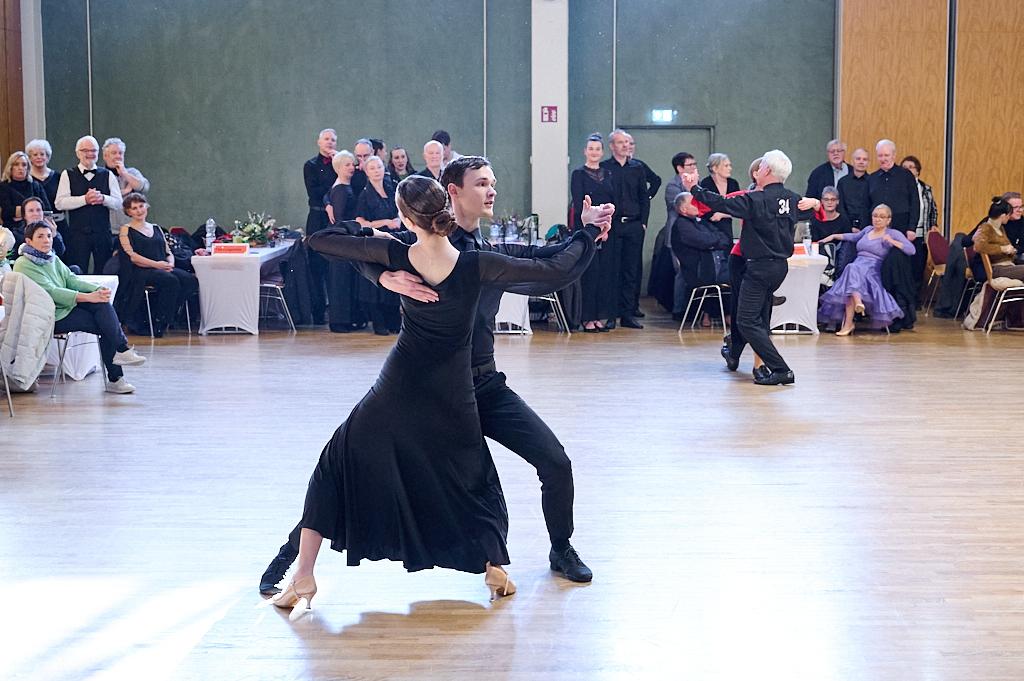 Tanzpaar in eleganter Kleidung f&uuml;hrt einen Ausdruckstanz auf, Zuschauer im Hintergrund applaudieren.