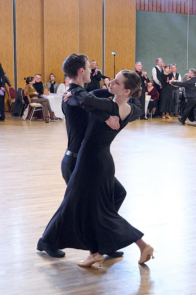 Tanzpaar in eleganter Kleidung f&uuml;hrt einen Paartanz in einem festlichen Saal mit applaudierendem Publikum aus.