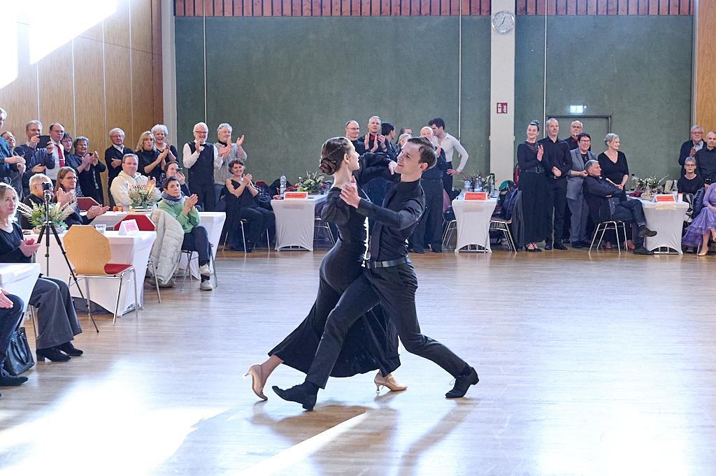 Tanzpaar in eleganter Kleidung f&uuml;hrt einen Tanz auf einer Veranstaltung; Publikum applaudiert im Hintergrund.