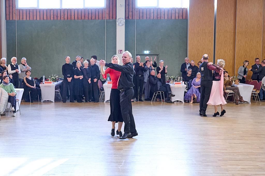 Tanzende Paare in eleganter Kleidung auf einer Tanzfl&auml;che, Zuschauer sitzen an Tischen im Hintergrund.