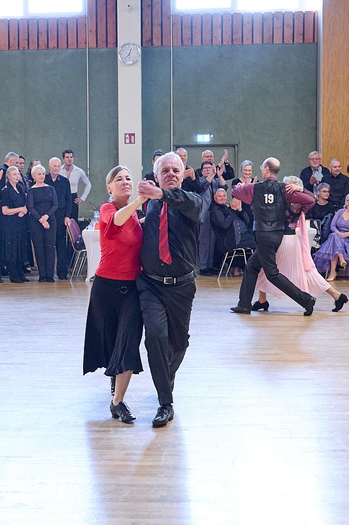 Tanzendes Paar in eleganter Kleidung auf einer Tanzfl&auml;che, Publikum beobachtet und applaudiert im Hintergrund.