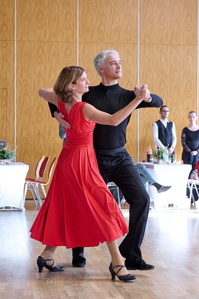 Tanzendes Paar in eleganter Kleidung, der Mann in Schwarz und die Frau im roten Kleid auf einer Tanzfl&auml;che.