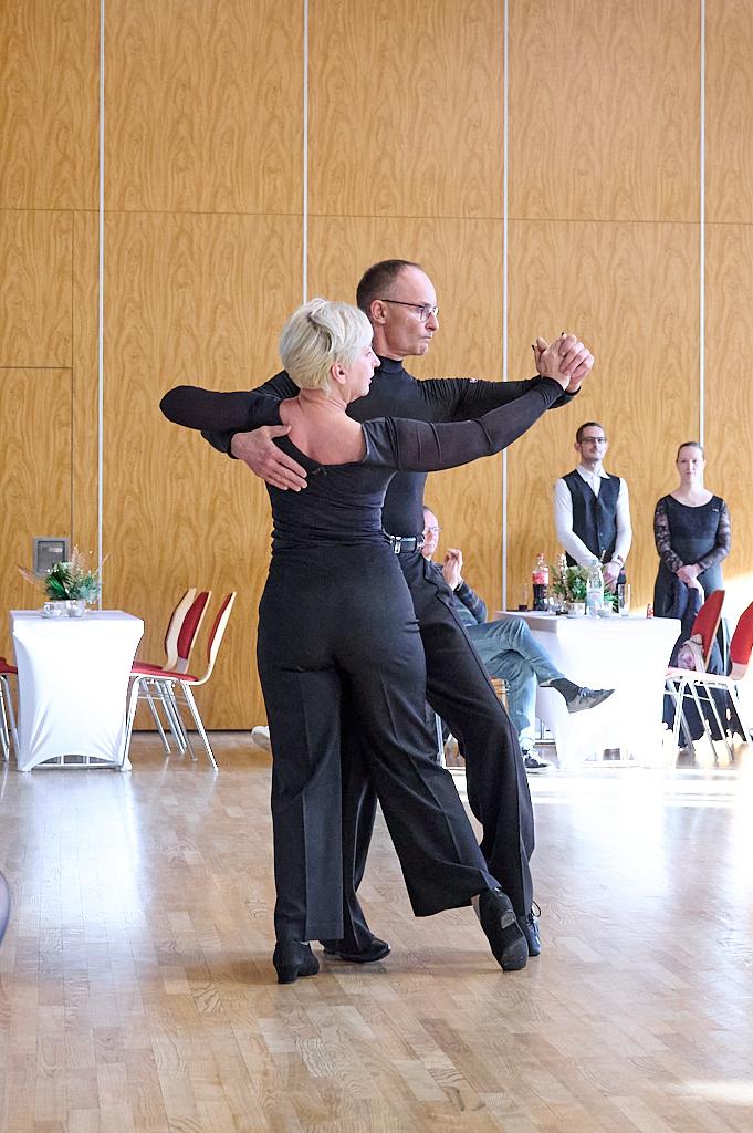 Tanzpaar in eleganter Haltung auf einer Tanzfl&auml;che; Zuschauer im Hintergrund beobachten die Darbietung.