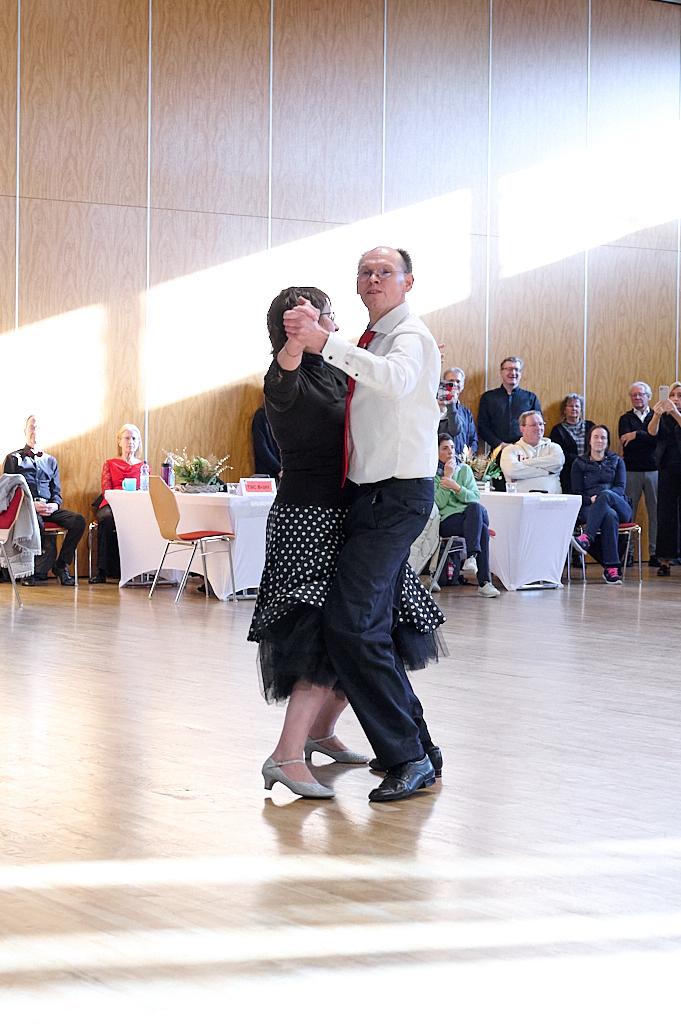 Tanzendes Paar in eleganter Kleidung auf einer hellen Tanzfl&auml;che, Zuschauer verfolgen aufmerksam.