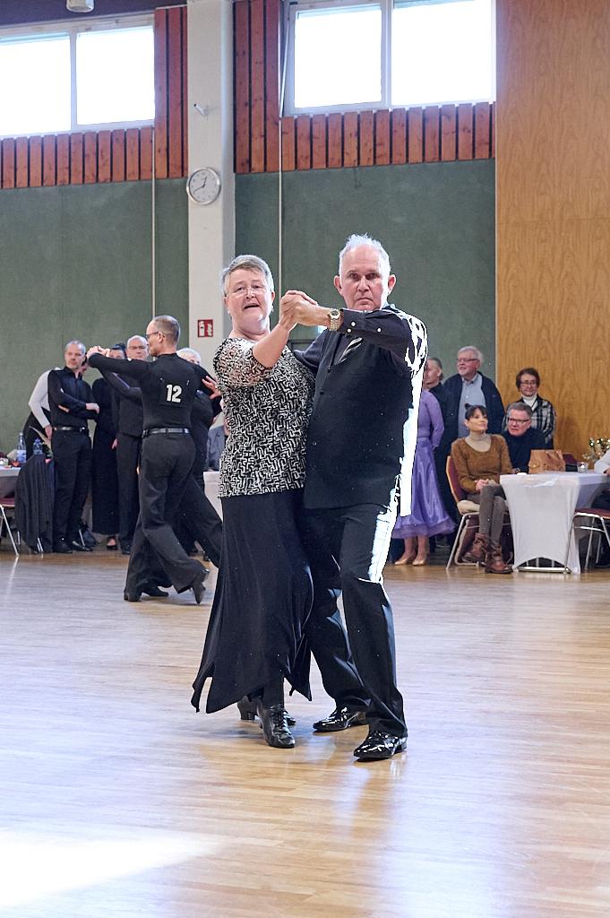 Tanzendes Paar in eleganter Kleidung auf einer Tanzfl&auml;che, im Hintergrund weitere T&auml;nzer und Zuschauer.