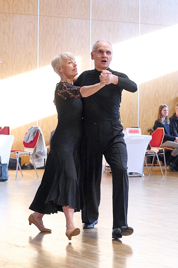 Tanzpaar in eleganter Kleidung f&uuml;hrt einen Paartanz auf einer Holzfu&szlig;bodenfl&auml;che in einem hellen Raum aus.