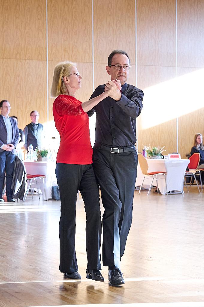 Tanzendes Paar in einem festlichen Saal, gehaltene H&auml;nde, Frauen in rotem Oberteil, Mann in schwarzem Hemd.