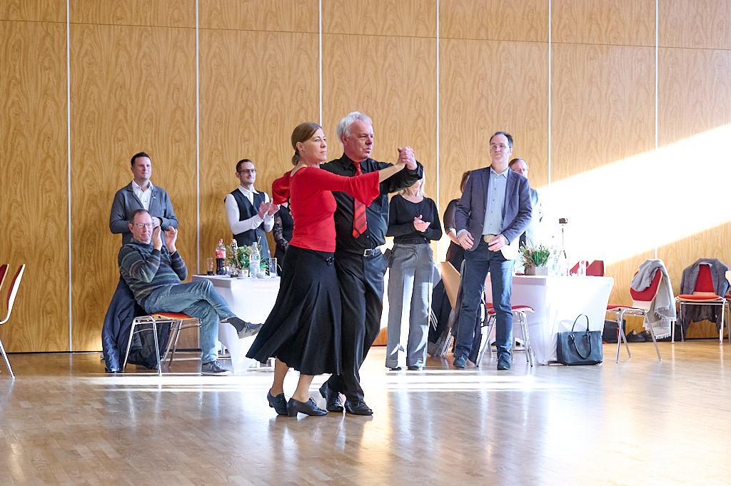 Tanzendes Paar in eleganter Kleidung, umgeben von applaudierenden G&auml;sten in einem festlichen Saal.