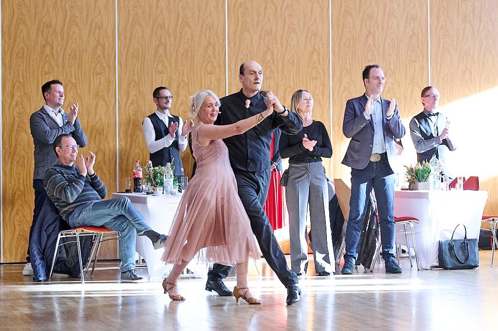 Tanzen eines Paares in eleganter Kleidung, umgeben von applaudierenden G&auml;sten in einem festlichen Raum.