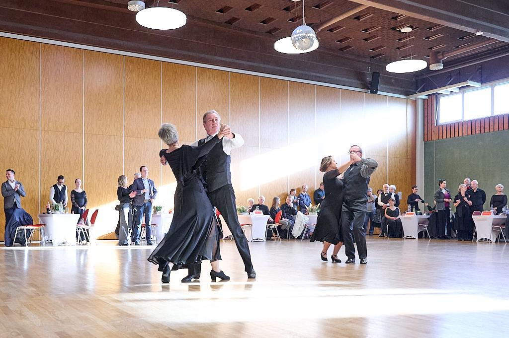 Tanzende Paare in eleganter Kleidung auf einer Tanzfl&auml;che, umgeben von G&auml;sten an festlich gedeckten Tischen.