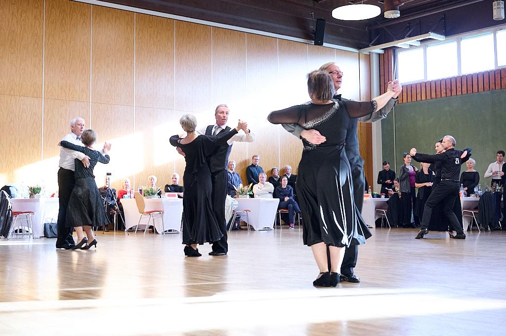 Tanzende Paare in formeller Kleidung auf einer Tanzfl&auml;che, mit G&auml;sten im Hintergrund an Tischen.