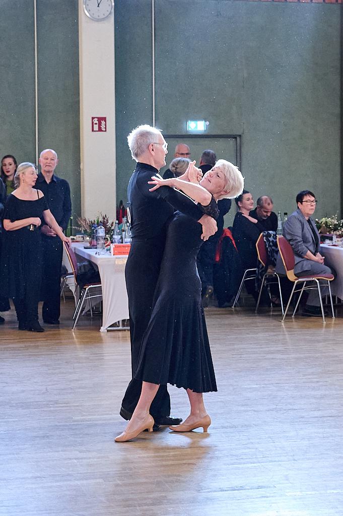 Tanzendes Paar in eleganter Kleidung auf einer Tanzfl&auml;che, im Hintergrund Zuschauer und Tischgedecke sichtbar.