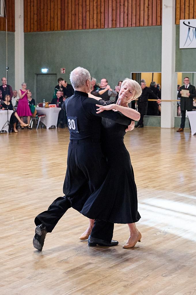 Tanzendes Paar in eleganter Kleidung auf einer Holzfl&auml;che, die sich anmutig umarmen und eine Tanzfigur ausf&uuml;hren.