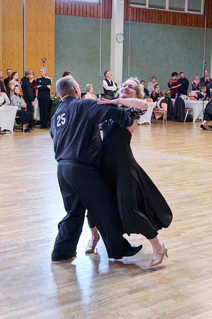 Tanzpaar in eleganter Kleidung f&uuml;hrt einen Walzer auf einer Tanzfl&auml;che vor einem Publikum aus G&auml;sten vor.
