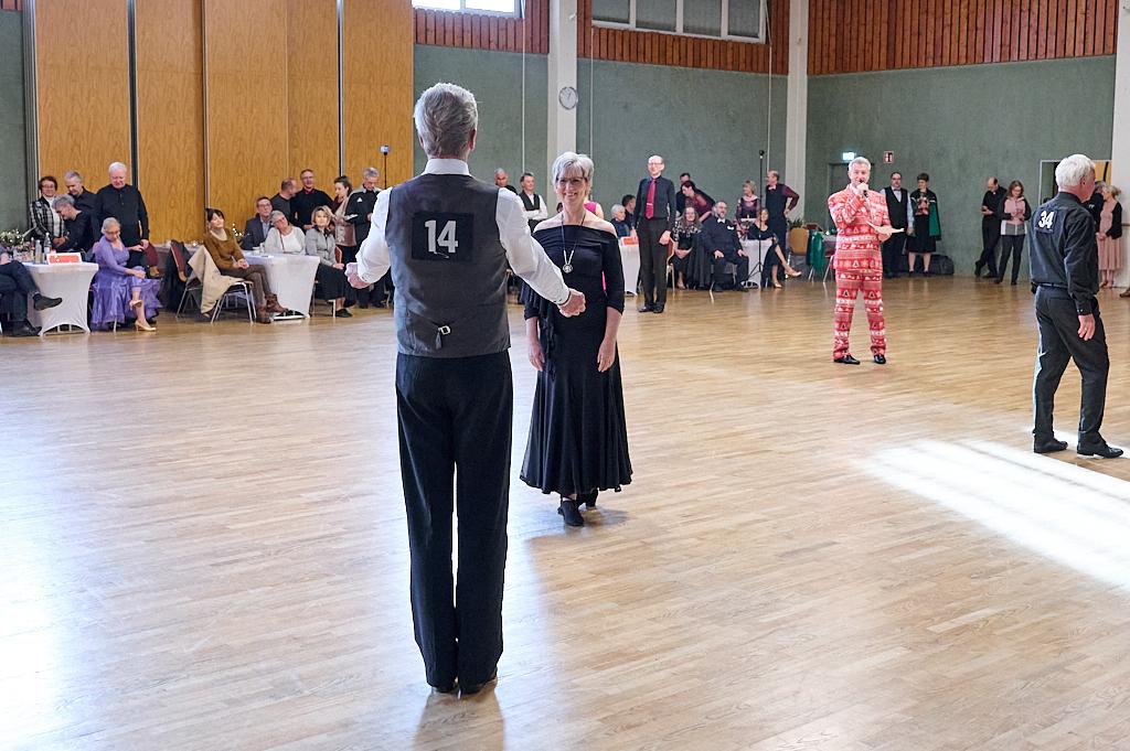 Tanzendende Paare in eleganter Kleidung auf einer Tanzfl&auml;che, im Hintergrund Zuschauer an Tischen.