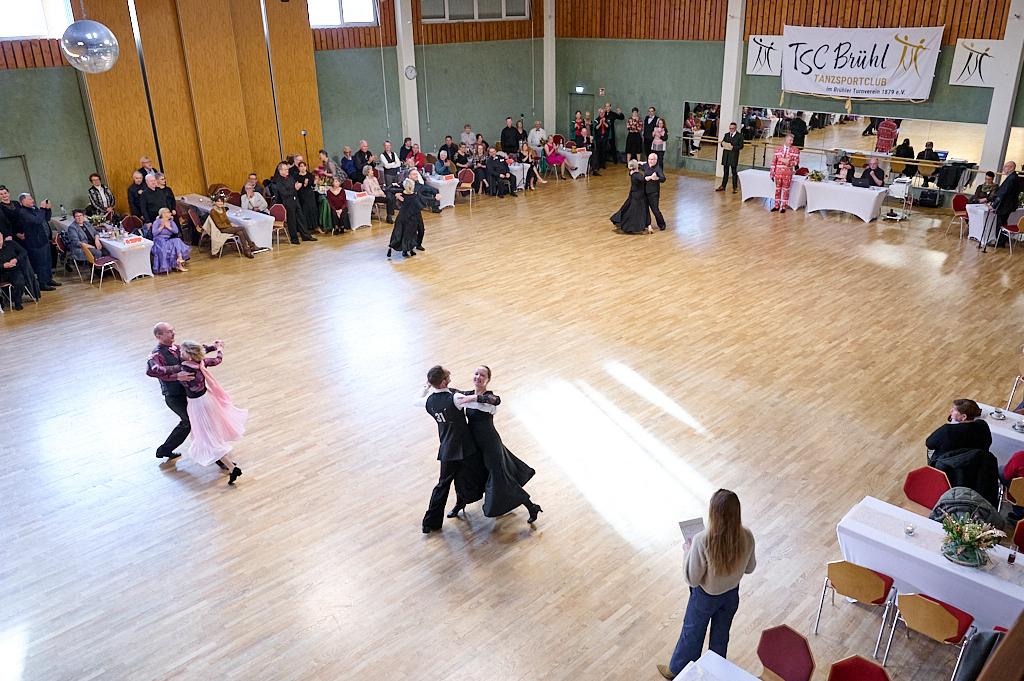 Tanzsportturnier im Saal mit t&auml;nzerischen Paaren und Publikum an Tischen, im Hintergrund eine Band und eine Banner.