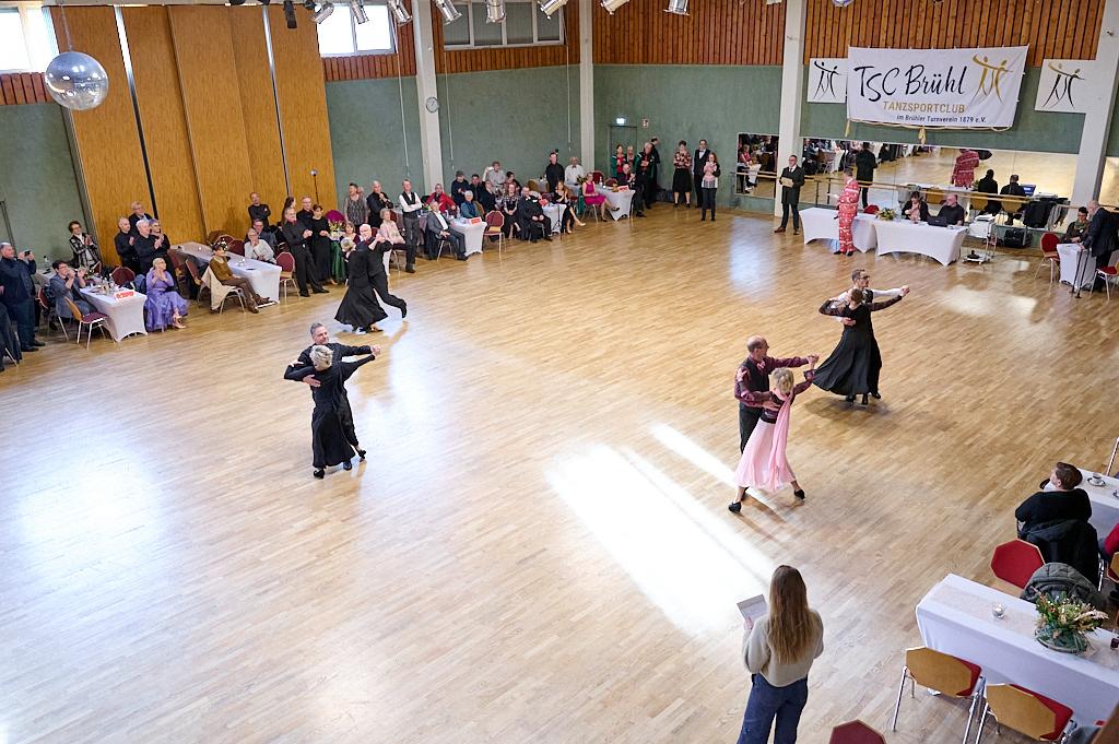 Tanzveranstaltung im TSC Br&uuml;hl mit mehreren Paaren, die auf einer Holzfl&auml;che tanzen, umgeben von Zuschauern.