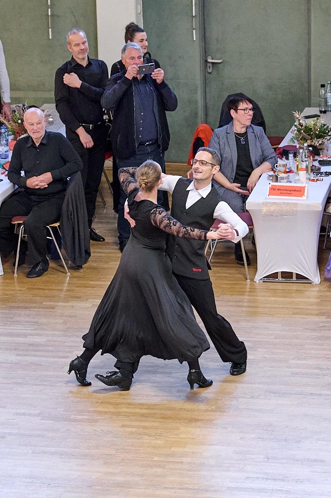 Tanzpaar in eleganter Kleidung tanzt leidenschaftlich auf einer Tanzfl&auml;che, umgeben von Zuschauern an festlich gedeckten Tischen.