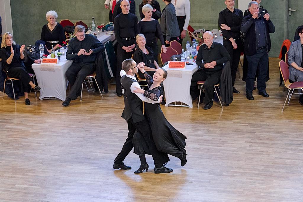 Tanzpaar in eleganter Kleidung tanzt auf einer Holzb&uuml;hne, w&auml;hrend das Publikum aufmerksam zusieht.