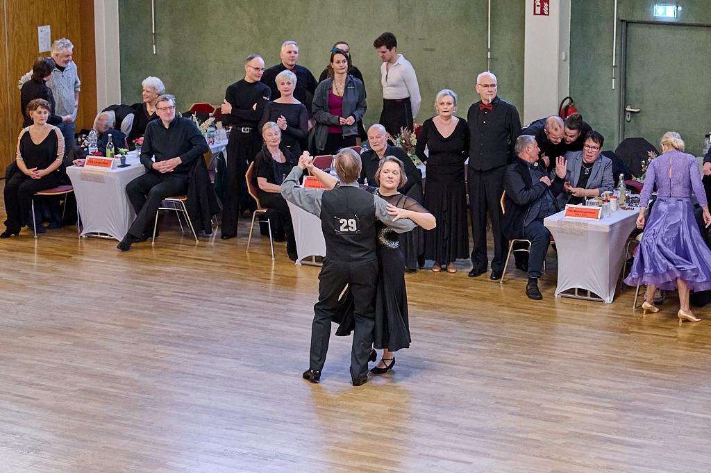 Tanzpaar in eleganter Kleidung w&auml;hrend eines Wettbewerbs, umgeben von zuschauenden G&auml;sten an festlich gedeckten Tischen.