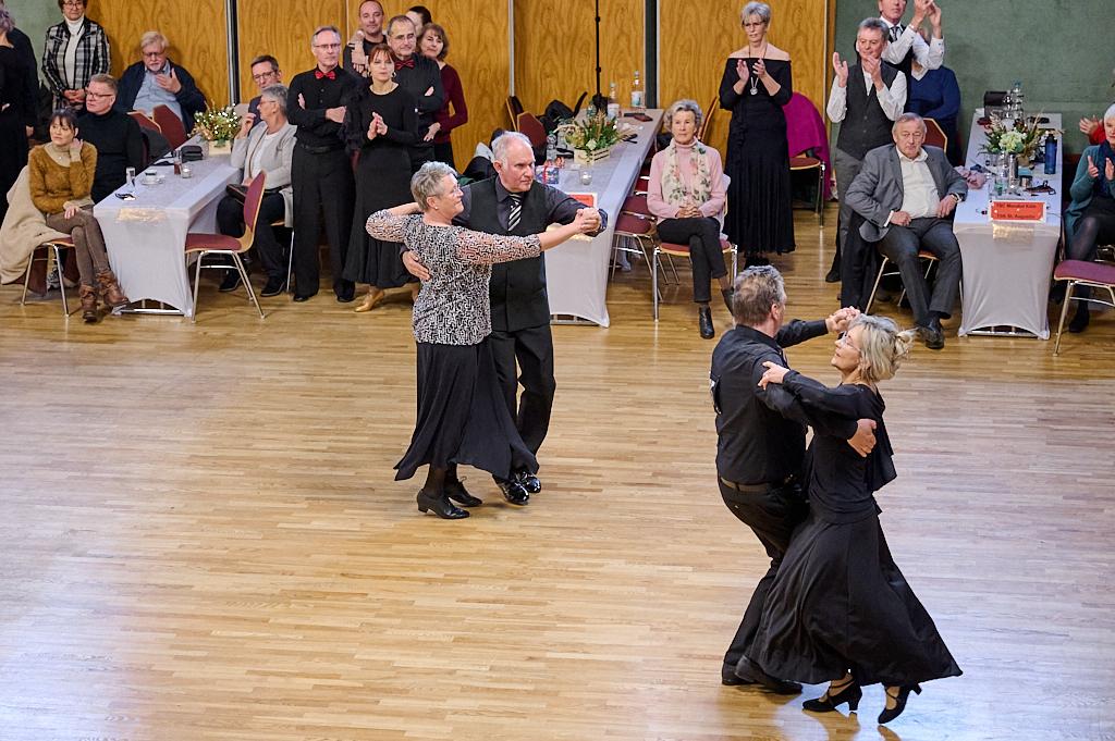 Tanzpaar in formeller Kleidung f&uuml;hrt einen Walzer auf einer Tanzfl&auml;che, umgeben von applaudierenden Zuschauern.