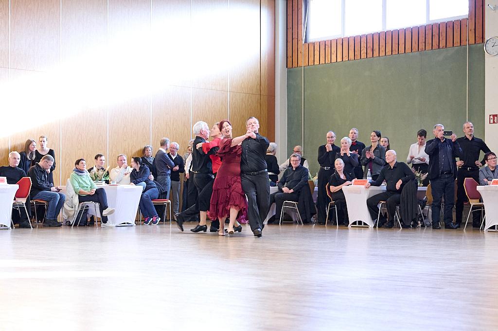 Tanzendes Paar in festlicher Kleidung auf einer Tanzfl&auml;che, umgeben von Zuschauern, die aufmerksam beobachten.