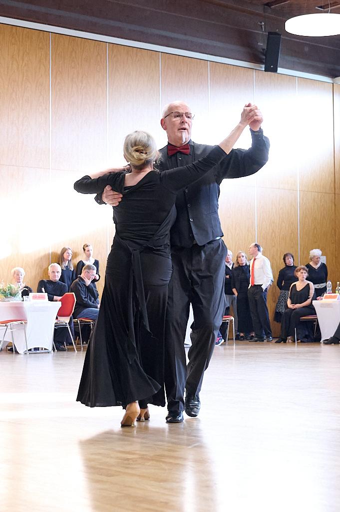 Tanzendes Paar in eleganter Kleidung auf einer Tanzfl&auml;che bei einer Veranstaltung, umgeben von sitzendem Publikum.
