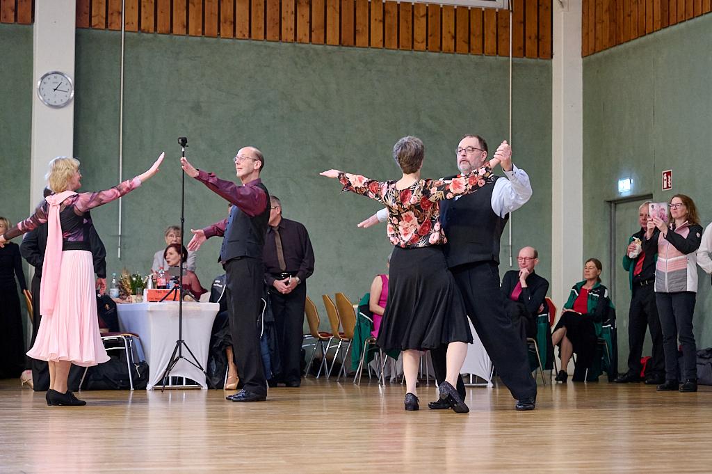 Tanzende Paare in eleganter Kleidung auf einer Tanzfl&auml;che, Zuschauer im Hintergrund applaudieren.