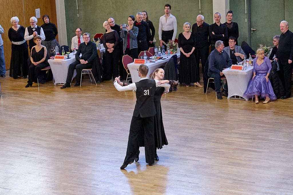 Tanzendes Paar in eleganter Kleidung bei einem Wettkampf, umgeben von zuschauenden G&auml;sten in festlicher Stimmung.