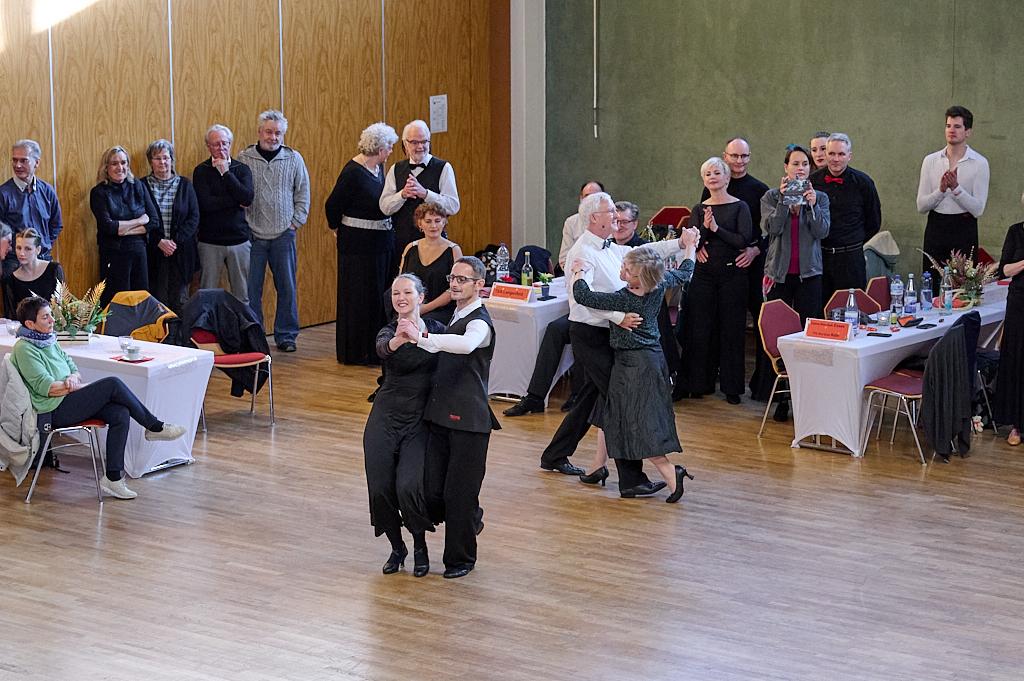 Tanzende Paare in eleganter Kleidung umgeben von zuschauenden G&auml;sten in einem festlichen Saal.