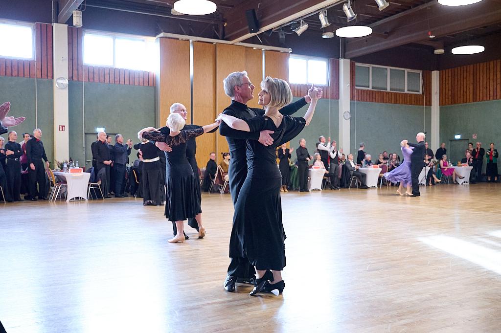 Tanzende Paare in eleganter Kleidung auf einer Tanzfl&auml;che, umgeben von Publikum in einem festlichen Saal.