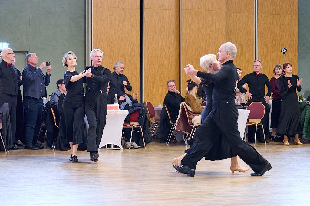 Tanzende Paare in schwarzer Kleidung auf einer Tanzfl&auml;che, umgeben von Zuschauern in einem festlichen Saal.