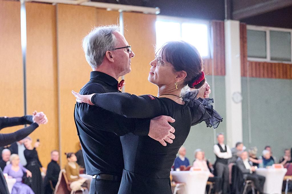 Tanzpaar in eleganter Kleidung w&auml;hrend eines Tanzwettbewerbs, umgeben von Zuschauern in einem Festsaal.