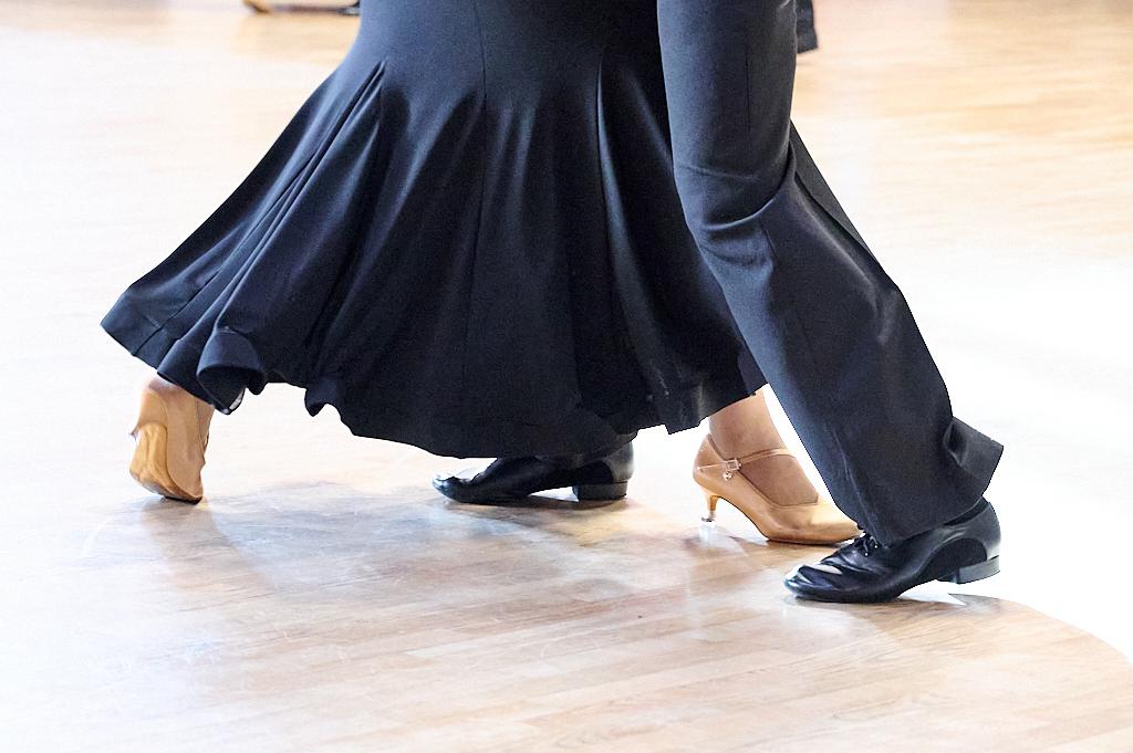 Tanzende Paare zeigen ihre F&uuml;&szlig;e, einer in schwarzen, der andere in beigen Schuhen auf glattem Parkettboden.