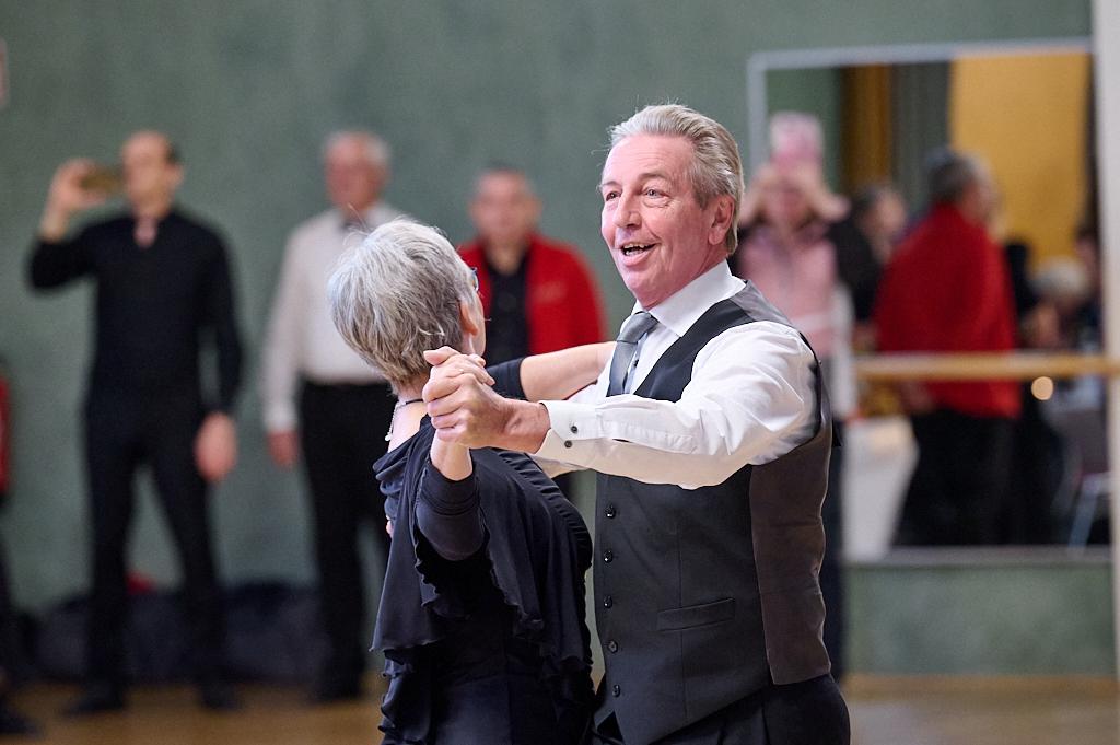 Tanzendes Paar in eleganter Kleidung, umgeben von Zuschauern in einem festlichen Veranstaltungsraum.