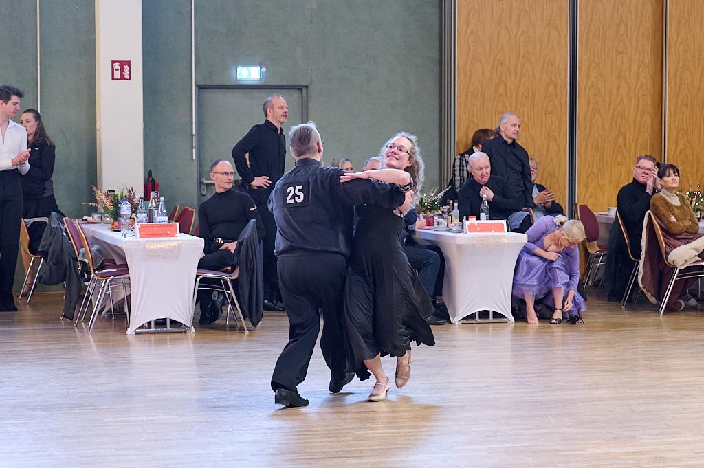 Tanzpaar in eleganter Kleidung tanzt in einem festlichen Saal, w&auml;hrend Zuschauer an Tischen beobachten.