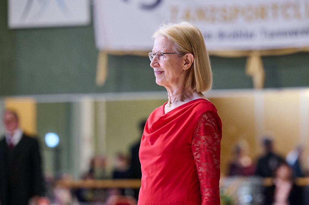 &Auml;ltere Dame in rotem Kleid steht l&auml;chelnd auf einer Tanzfl&auml;che w&auml;hrend einer Tanzveranstaltung.