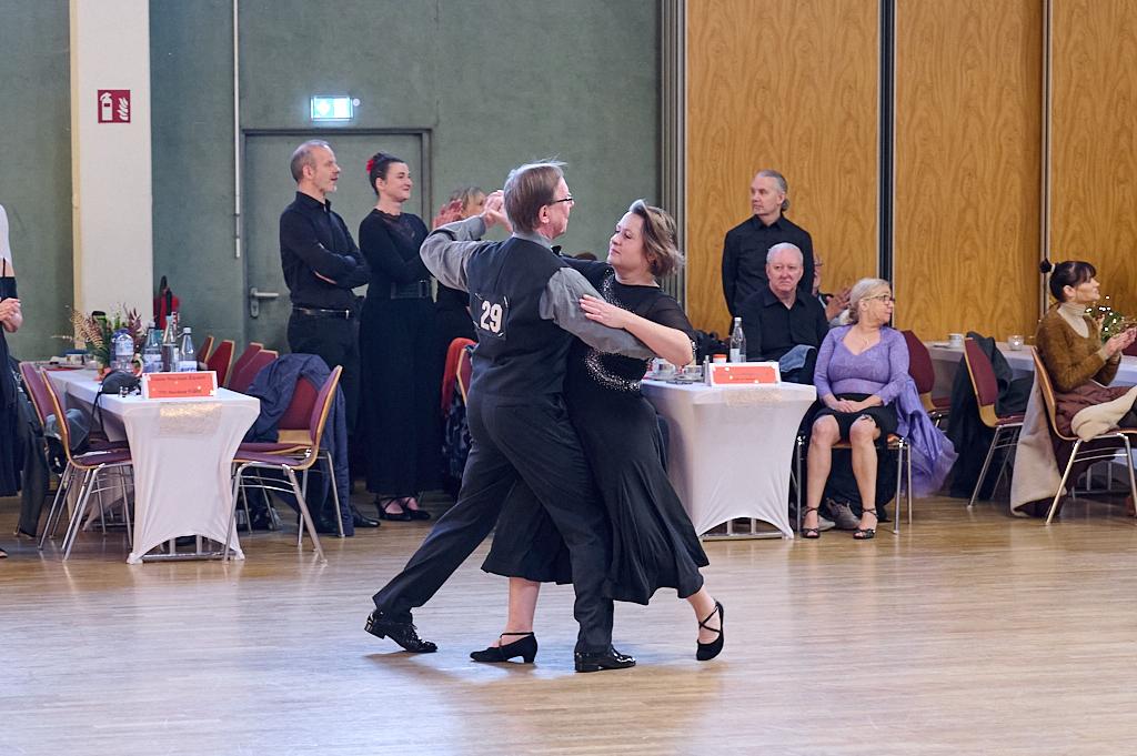 Tanzendes Paar in eleganter Kleidung auf einer Tanzfl&auml;che, umgeben von Zuschauern und Tischen.