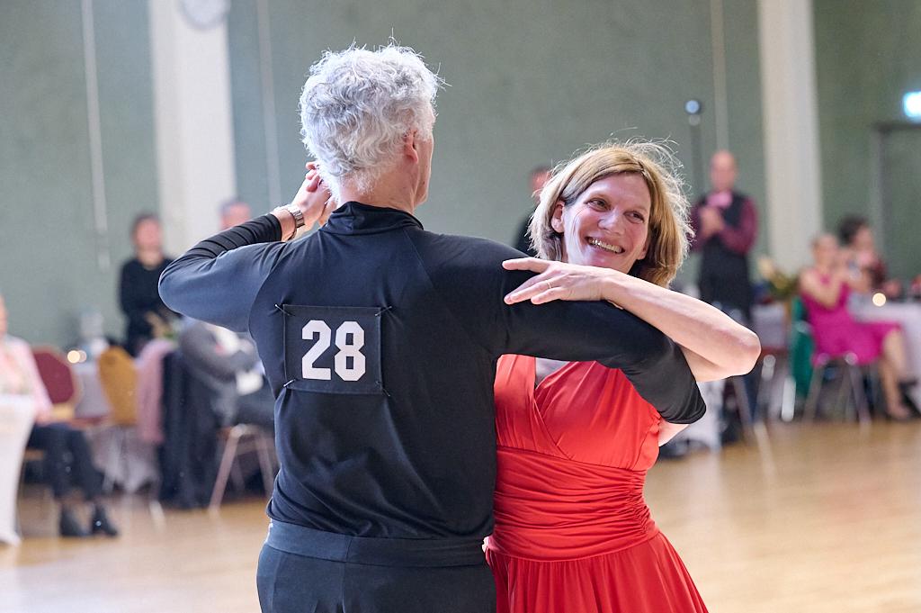 Tanzpaar inmitten eines Festsaals, der Mann tr&auml;gt eine schwarze Kleidung mit der Nummer 28, die Frau ein rotes Kleid.