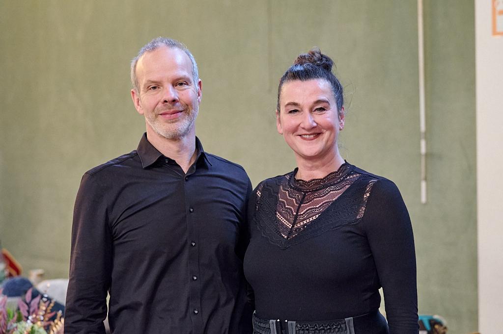 Portr&auml;t von einem Mann in schwarzem Hemd und einer Frau in schwarzem Oberteil mit Spitze, beide l&auml;cheln freundlich.