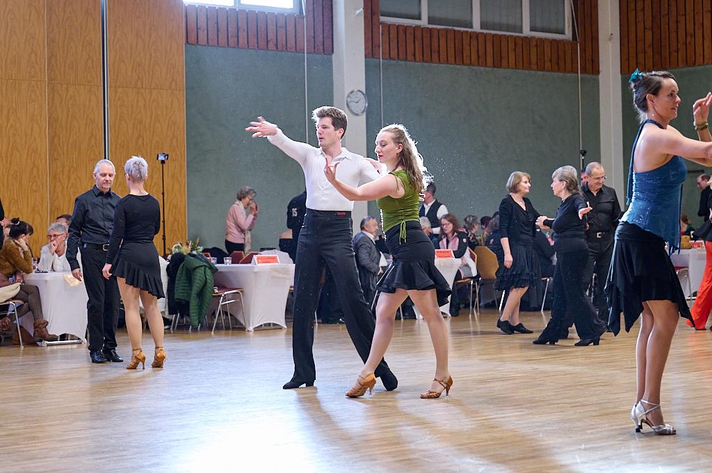 Tanzveranstaltung mit Paaren in eleganter Kleidung, die auf einer Tanzfl&auml;che zu Musik tanzen. Tische im Hintergrund.