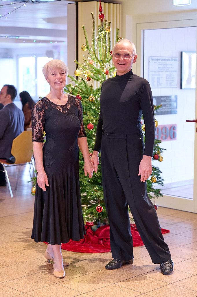 Tanzendes Paar in eleganter Kleidung steht vor einem geschm&uuml;ckten Weihnachtsbaum in festlicher Atmosph&auml;re.