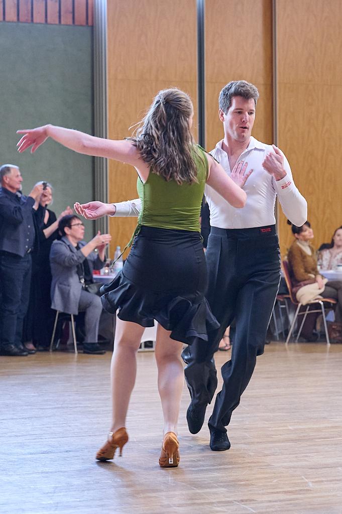 Tanzendes Paar in elegantem Outfit auf einer Tanzfl&auml;che, umgeben von Zuschauern bei einer Veranstaltung.