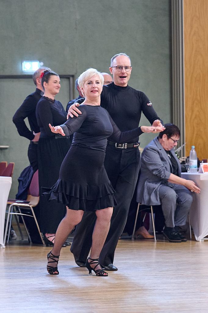 Tanzende Paare in eleganter Kleidung, Hintergrund mit Zuschauern und einer festlichen Atmosph&auml;re.