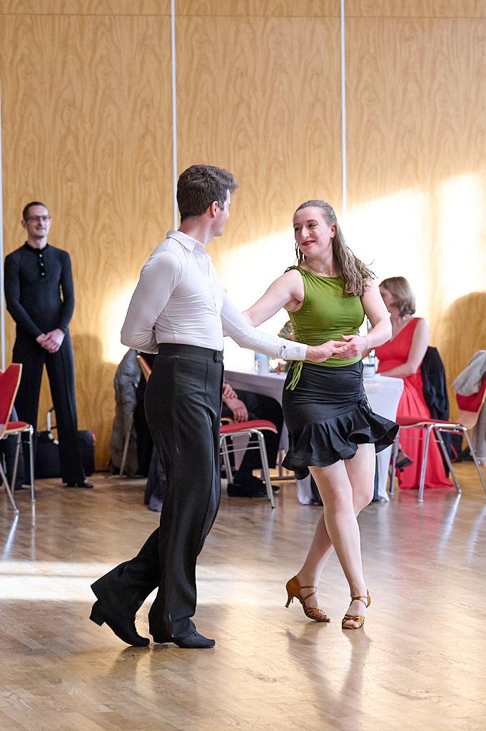 Tanzpaar in eleganter Kleidung bei einem Tanzwettbewerb, umgeben von Zuschauern in einem festlichen Saal.