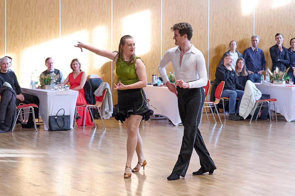 Tanzpaar in auff&auml;lliger Kleidung pr&auml;sentiert einen Paso Doble in einem hellen Saal vor einer Zuschauergruppe.