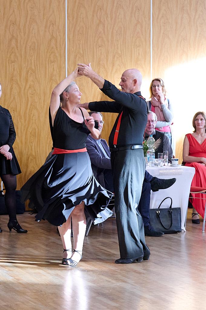 Tanzendes Paar in eleganter Kleidung auf einer Veranstaltung, umgeben von Zuschauern und festlicher Dekoration.