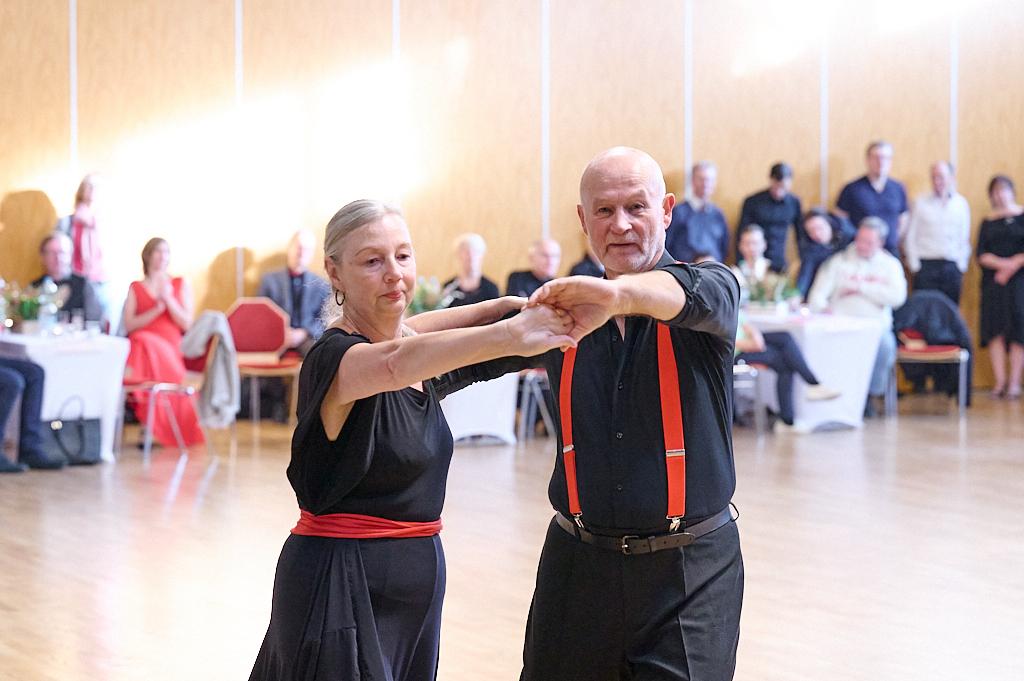 Tanzendes Paar in eleganter Kleidung, umgeben von Zuschauern in einem Veranstaltungsraum.