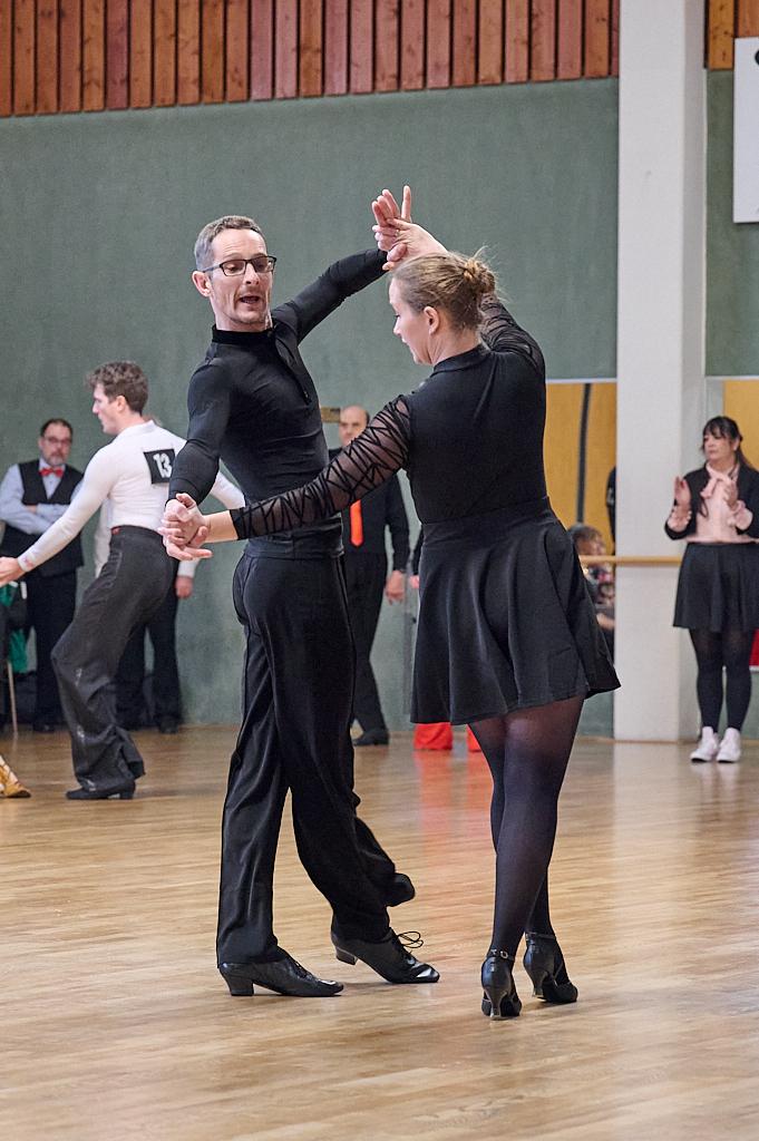 Tanzpaar in eleganter Kleidung, das auf einer Tanzfl&auml;che zu einem Wettbewerb tanzt. Zuschauer im Hintergrund applaudieren.